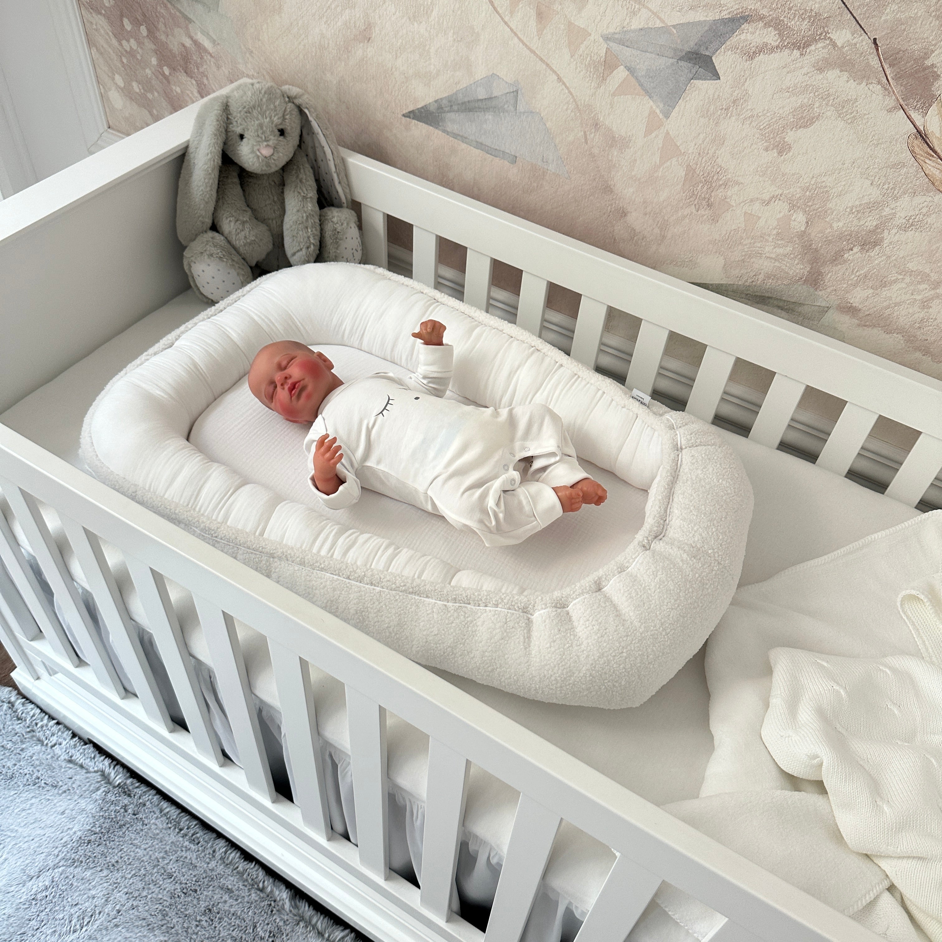 Baby liegt im Babynest Boucle weiß im Babybett Royal