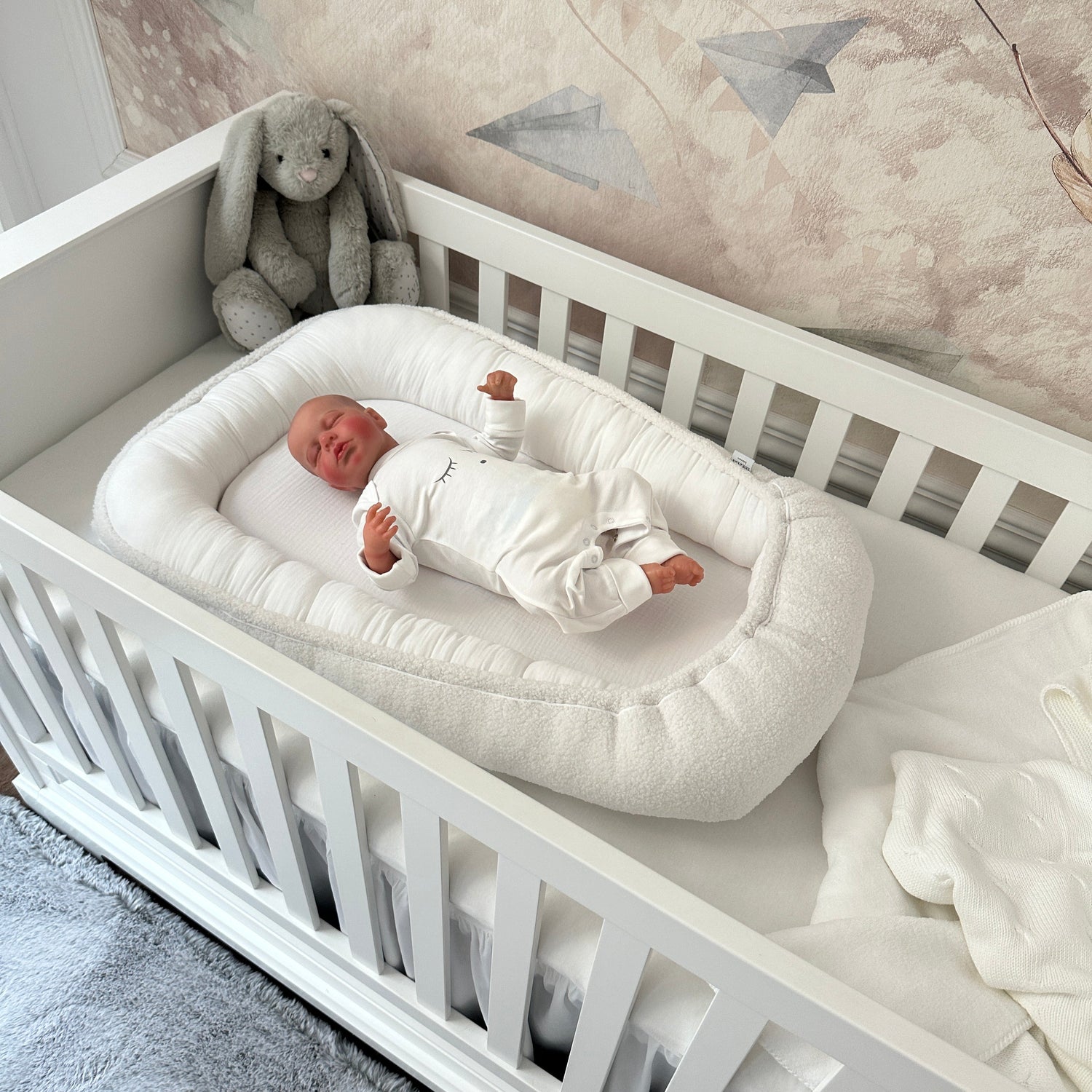 Baby liegt im Babynest Boucle weiß im Babybett Royal