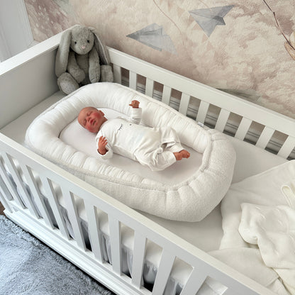 Baby liegt im Babynest Boucle weiß im Babybett Royal